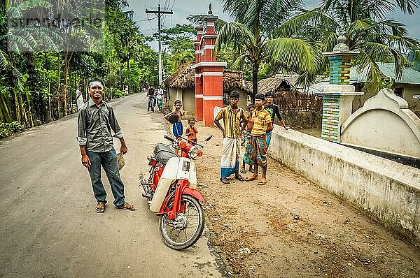 Paigacha  Bangladesch  etwa im Juli 2012: Junge einheimische Jungen stehen mit einem weiß roten Motorrad auf der Straße und lächeln in die Kamera in Paigacha  Bangladesch. Dokumentarischer Leitartikel  Asien