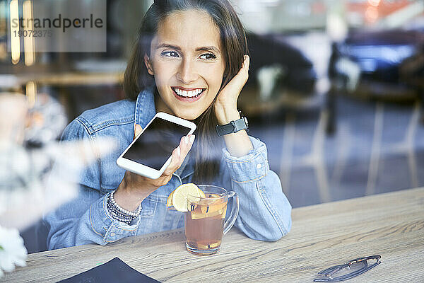 Lächelnde junge Frau telefoniert im Café  während sie Tee trinkt