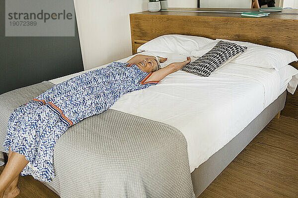 Glückliche reife Frau entspannt sich auf dem Bett in der Wohnung