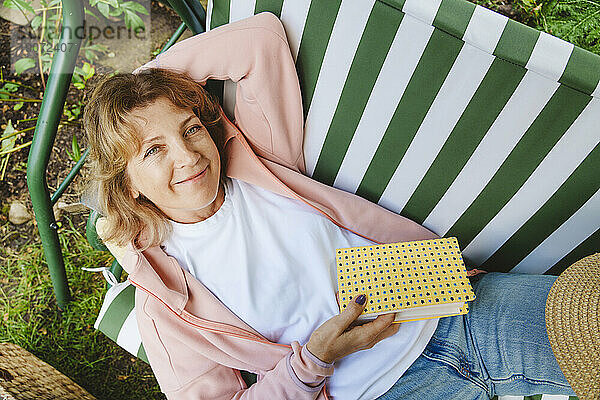 Smiling mature woman lying on swing with book