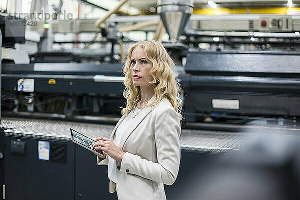 Frau mit Tablet an der Maschine in der Fabrikhalle und schaut sich um