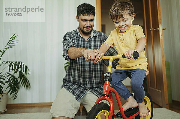 Vater hilft lächelndem Sohn  zu Hause Fahrrad zu fahren