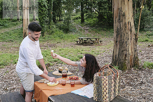 Frau gibt ihrem Freund Essen  der am Tisch im Wald steht