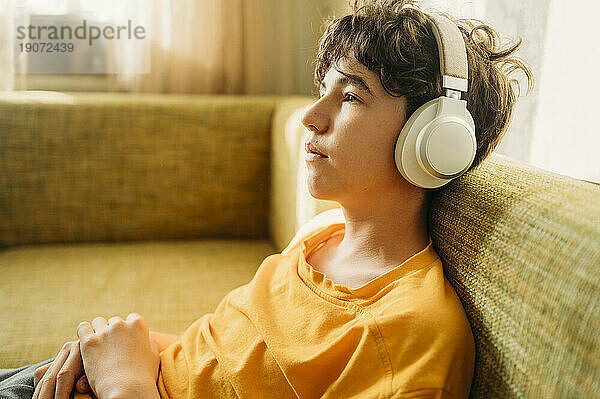 Nachdenklicher Junge mit Kopfhörern entspannt sich auf dem Sofa