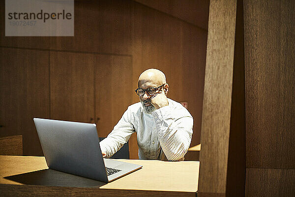 Portrait of mature man working on laptop at workspace with wood panelling