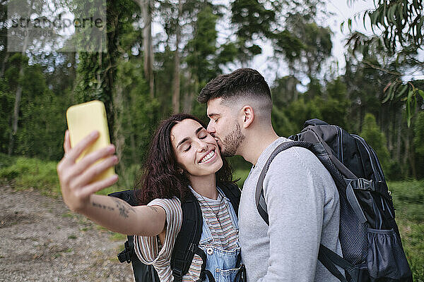 Man kissing girlfriend taking selfie through smart phone