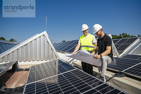 Zwei Techniker besprechen den Plan für das Dach eines Firmengebäudes mit Solarpaneelen
