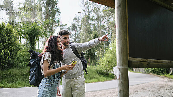 Mann zeigt auf Freundin  die Smartphone am Straßenrand hält