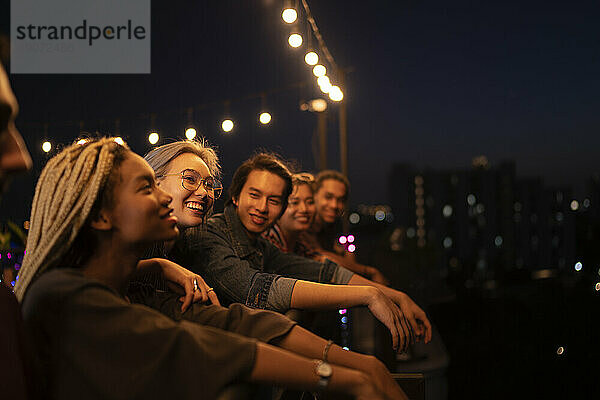 Smiling friends spending leisure time on rooftop at night