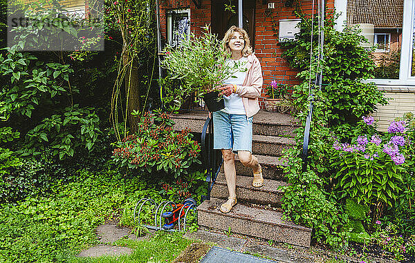 Lächelnde reife Frau  die mit Pflanzen eine Treppe hinuntersteigt