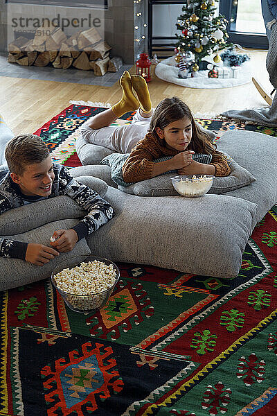 Lächelnder Junge  der Popcorn von seiner Schwester isst und zu Hause fernsieht