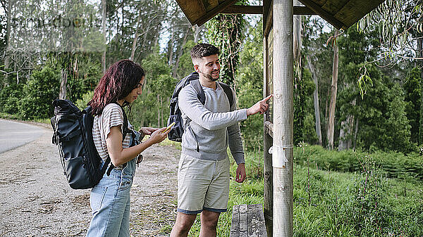 Mann zeigt auf Karte und steht mit Freundin am Smartphone