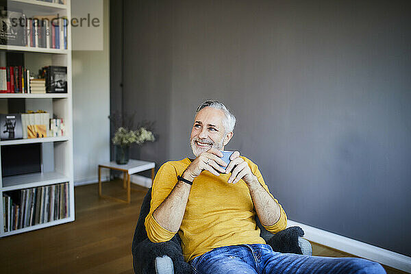 Smiling relaxed mature man at home with cup of coffee