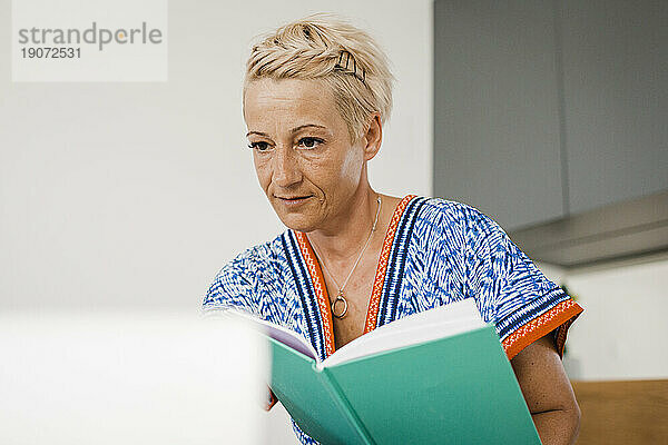 Frau mit Buch und Laptop im Schlafzimmer