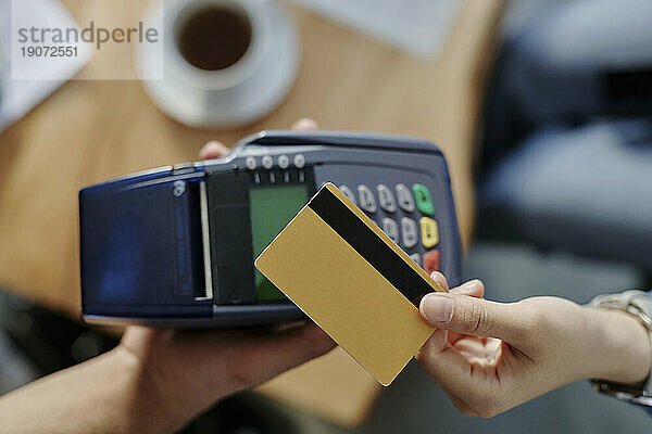 Hand of woman paying through credit card at cafe