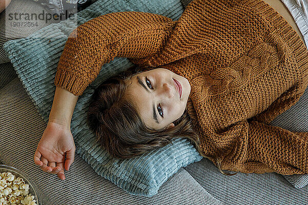 Smiling girl wearing knitted sweater and lying on pillows at home