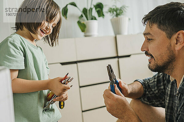 Smiling father and son holding hand tools at home