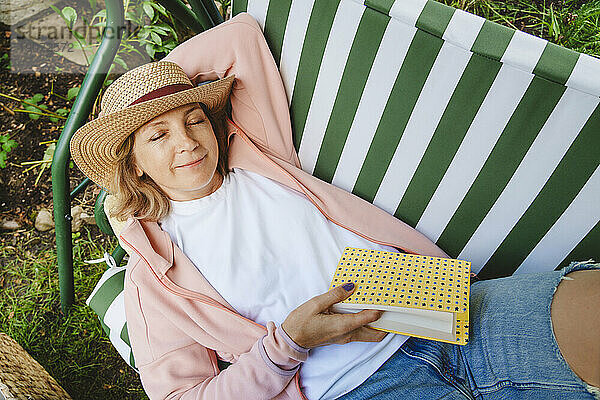 Lächelnde Frau mit Buch entspannt auf grüner Schaukel