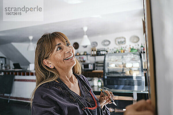 Lächelnder Cafébesitzer steht mit Stift im Café