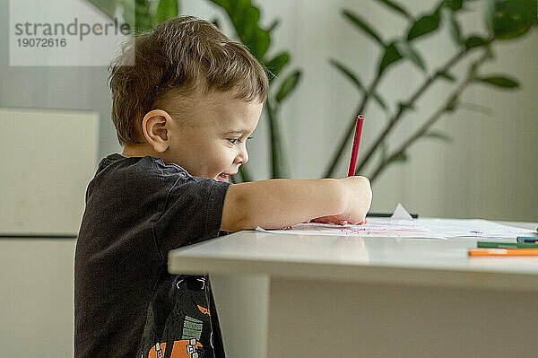 Lächelnder Junge  der zu Hause auf Papier malt