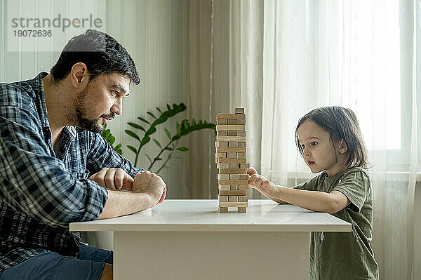 Sohn spielt Jenga mit Vater zu Hause am Tisch