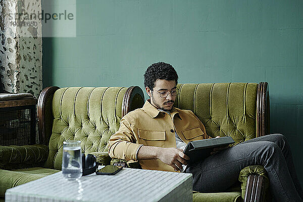 Junger Geschäftsmann sitzt entspannt im grünen Sessel und benutzt Tablet-PC