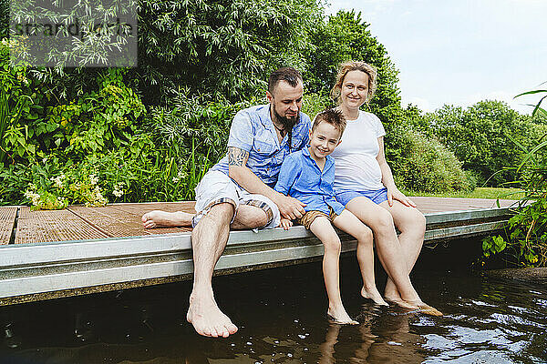Schwangere Frau verbringt ihre Freizeit mit ihrer Familie auf einem Steg über dem See