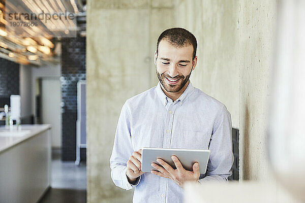 Lächelnder Geschäftsmann mit Tablet im modernen Büro