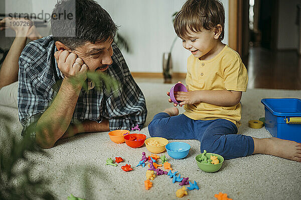 Lächelnder Vater und Sohn spielen zu Hause mit Plastikspielzeug