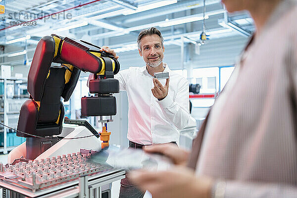 Geschäftsmann zeigt Geschäftsfrau Werkstück in einer modernen Fabrikhalle