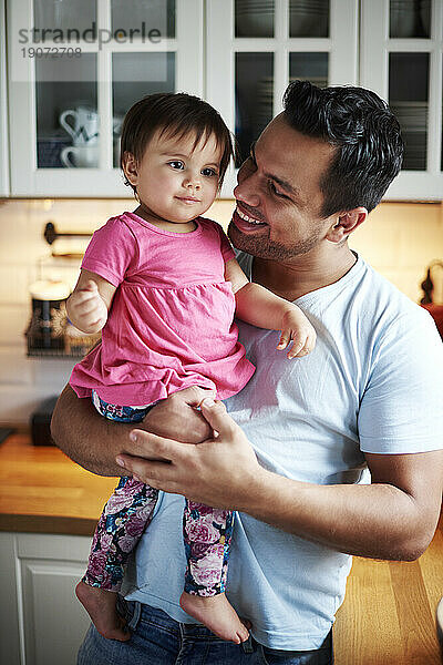 Lächelnder Vater hält sein kleines Mädchen zu Hause in der Küche