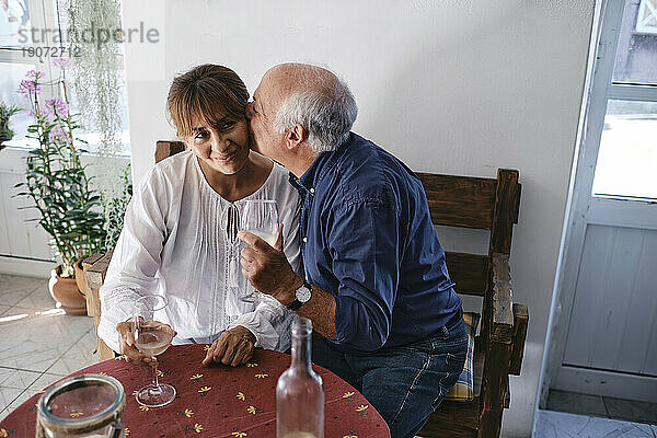 Glücklicher älterer Mann küsst Frau mit Gläsern Wein im Café