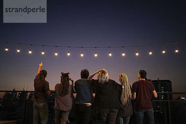 Freunde verbringen in der Abenddämmerung ihre Freizeit unter Lichterketten auf dem Dach