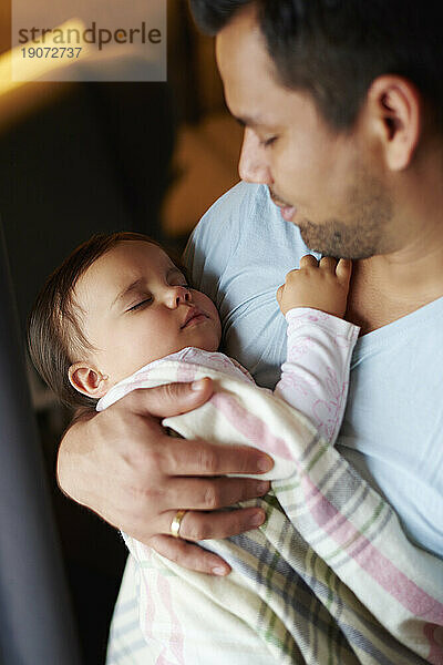 Zärtlicher Vater blickt auf sein kleines Mädchen  das in seinen Armen schläft