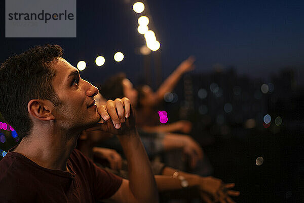 Contemplative man with friends staring at sky on rooftop at night