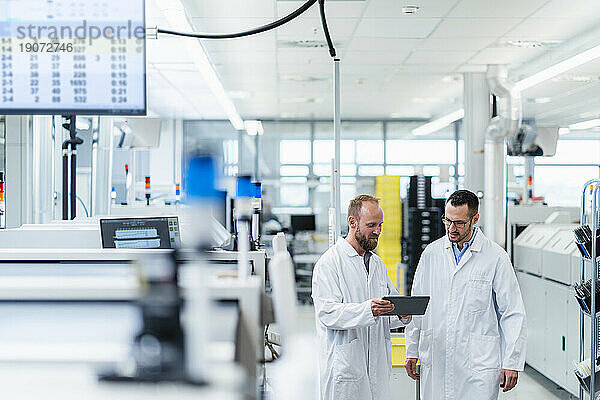 Zwei Kollegen schauen bei einem Arbeitstreffen in einer Elektronikfabrik auf ein digitales Tablet