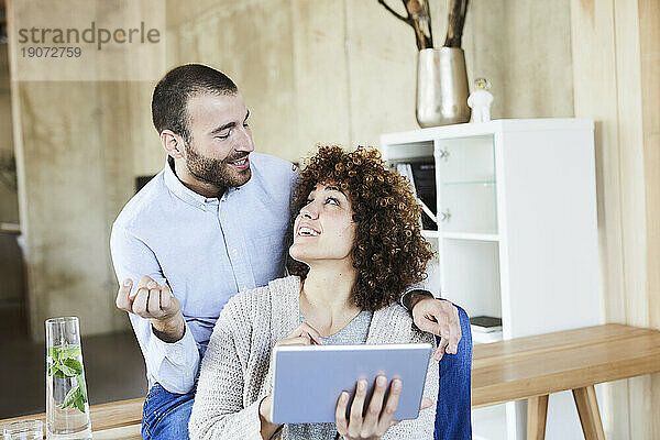 Glücklicher Mann und Frau mit Tablet unterhalten sich im modernen Büro
