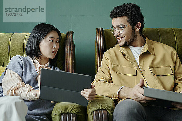Junge Geschäftspartner sitzen auf Sesseln und diskutieren mit Tablet-PC im Café