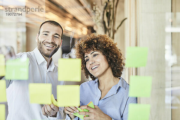 Zwei glückliche Kollegen beim Brainstorming mit Post-its auf einer Glasscheibe