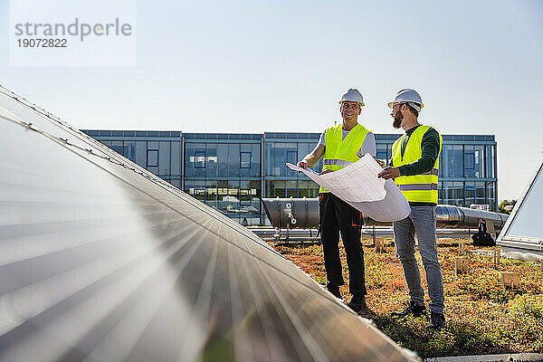 Zwei Techniker studieren den Plan auf dem Dach eines Firmengebäudes mit Solarpaneelen