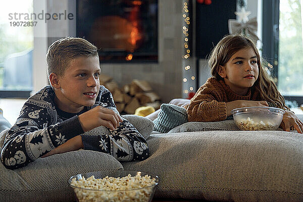 Bruder und Schwester essen Popcorn und schauen im Wohnzimmer fern