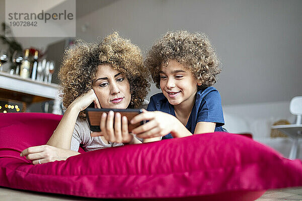 Mother and son watching a video on smartphone  lying on big pillow