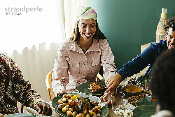Lächelnde Freunde beim Thanksgiving-Mittagessen am Esstisch
