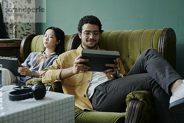 Geschäftsleute sitzen entspannt in Sesseln im Café und nutzen einen Tablet-PC