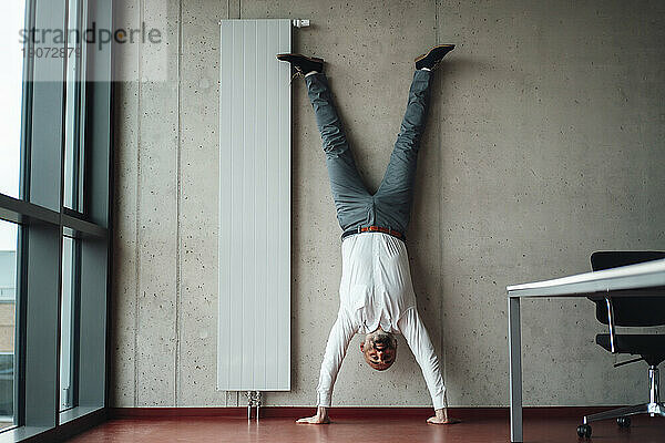 Geschäftsmann übt Handstand vor der Wand