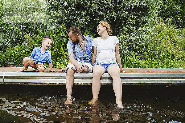 Glückliche schwangere Frau verbringt ihre Freizeit mit der Familie auf der Fußgängerbrücke über dem See
