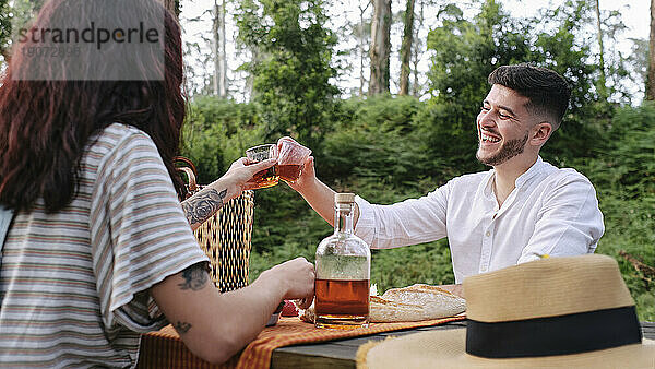 Fröhliches junges Paar genießt Getränke im Wald