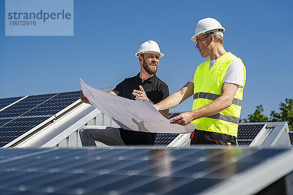 Zwei Techniker besprechen den Plan für das Dach eines Firmengebäudes mit Solarpaneelen