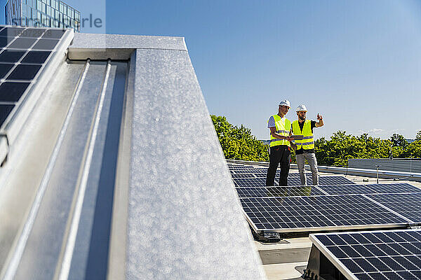 Zwei Techniker nutzen Tablet-PC auf dem Dach eines Firmengebäudes mit Solarpaneelen