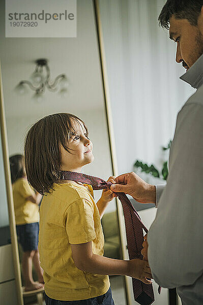 Father assisting son to adjust tie at home